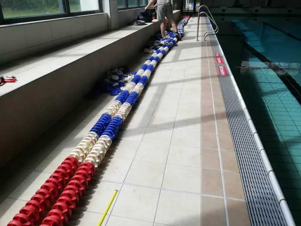 Eine erneuerte Wellenkiller-Leine mit roten, weißen und blauen Schwimmkörpern am Beckenrand