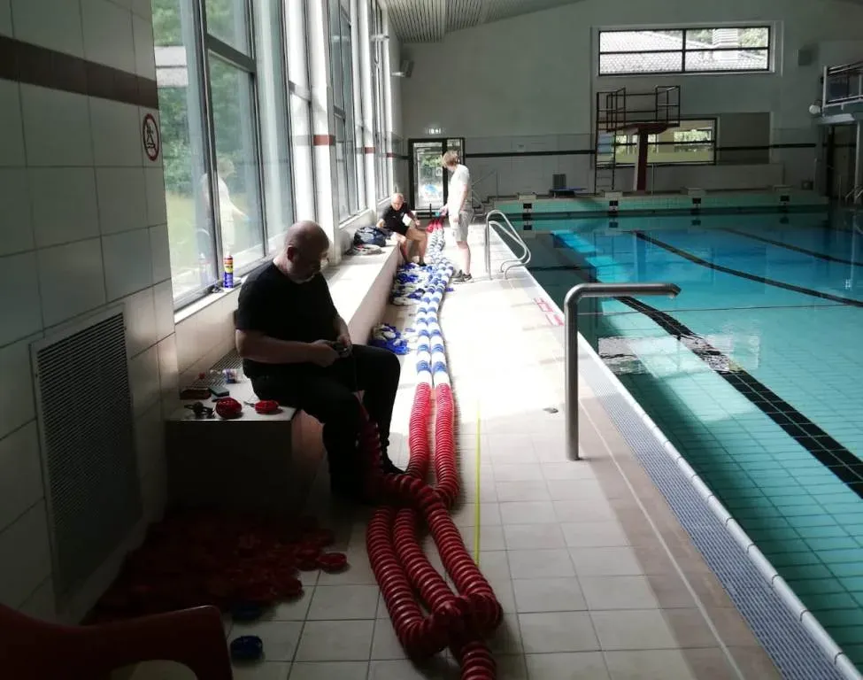 Vereinsmitglieder ziehen die Schwimmkörper auf die neuen Leinen, daneben das Becken