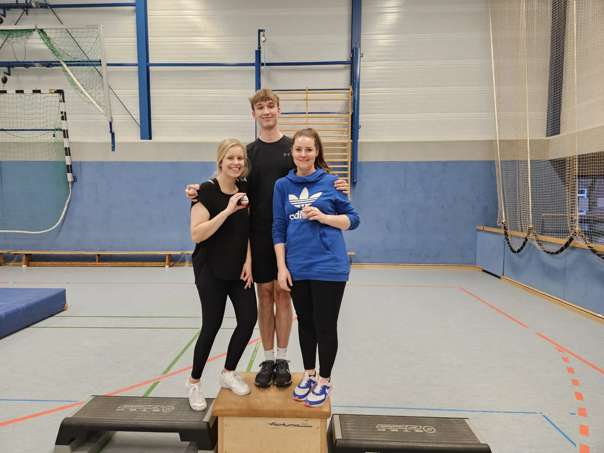 Drei Teilnehmende der Fortbildung auf einem Podest in der Sporthalle